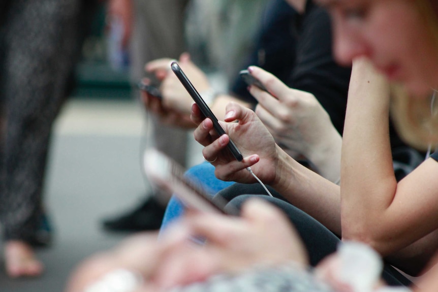 People sitting on a bench looking at their mobile phones