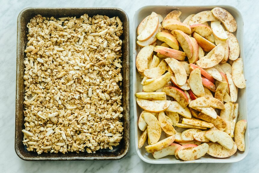 Crisp topping with nuts and oats on a baking tray besides a baking dish of chai spiced apples.