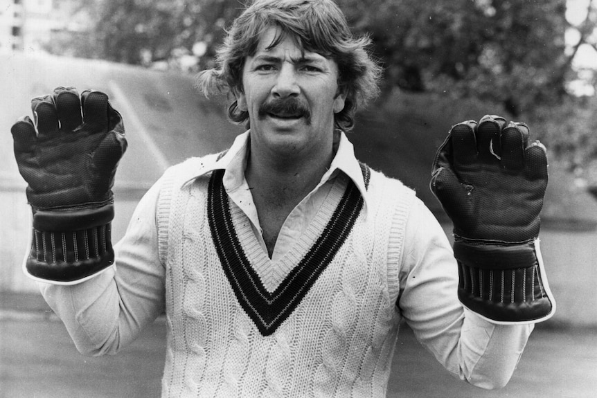 Rod Marsh smiles while holding up his hands while wearing wicketkeeping gloves