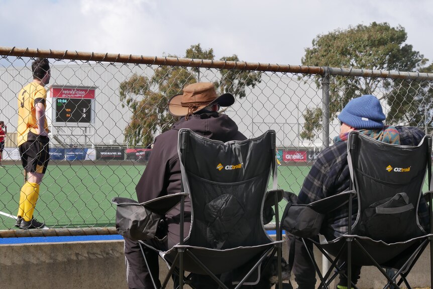 Two people in camp chairs watch a hockey match