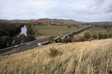 Ariel view of a beam bridge running over a river, mountains in the distance.