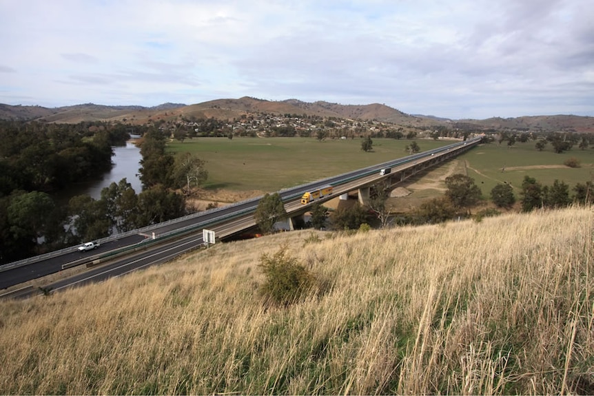 Ariel view of a beam bridge running over a river, mountains in the distance.