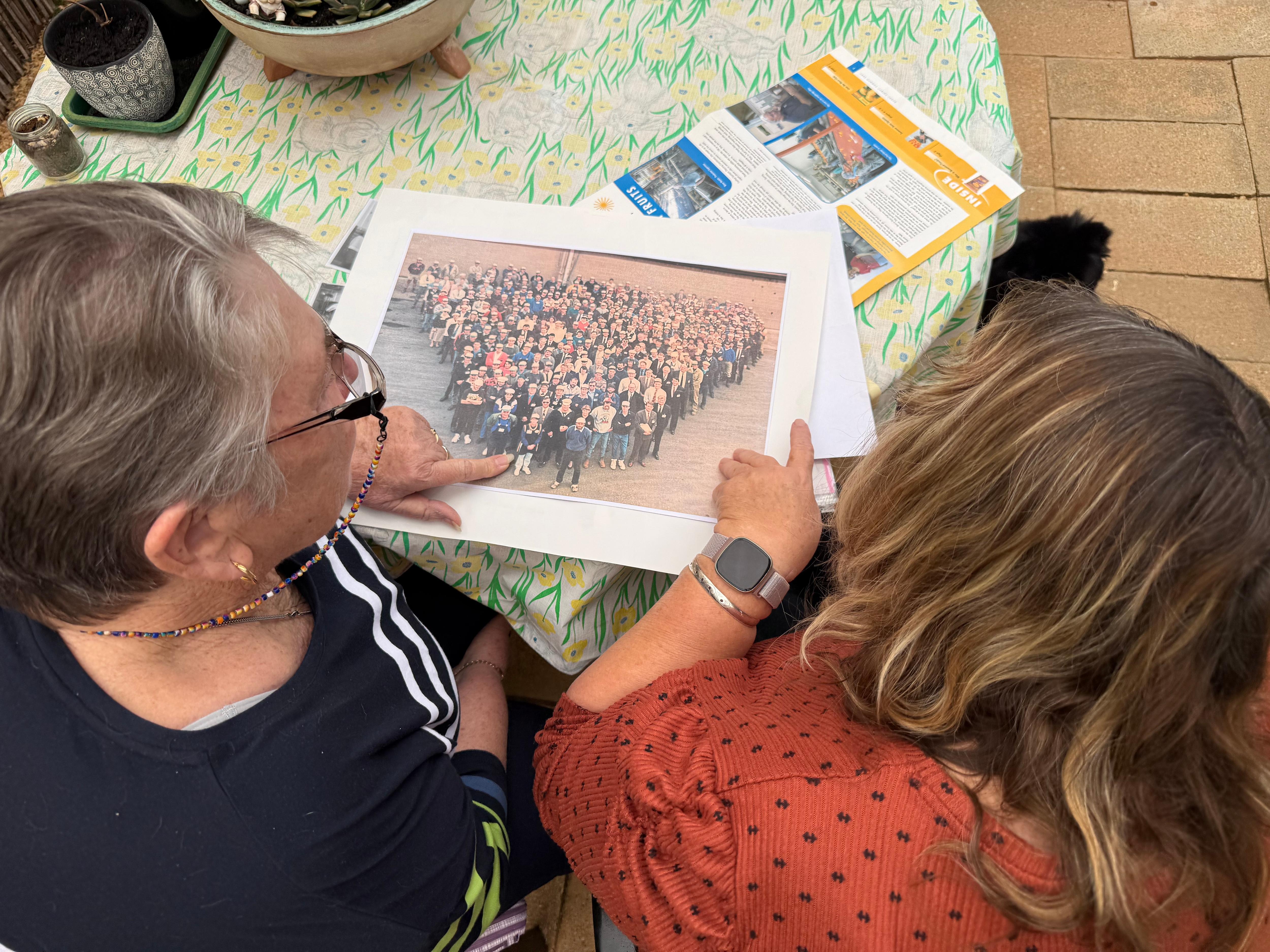 Two women look at an old group photo on a table