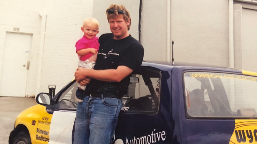 Father and baby daughter standing beside a rally car