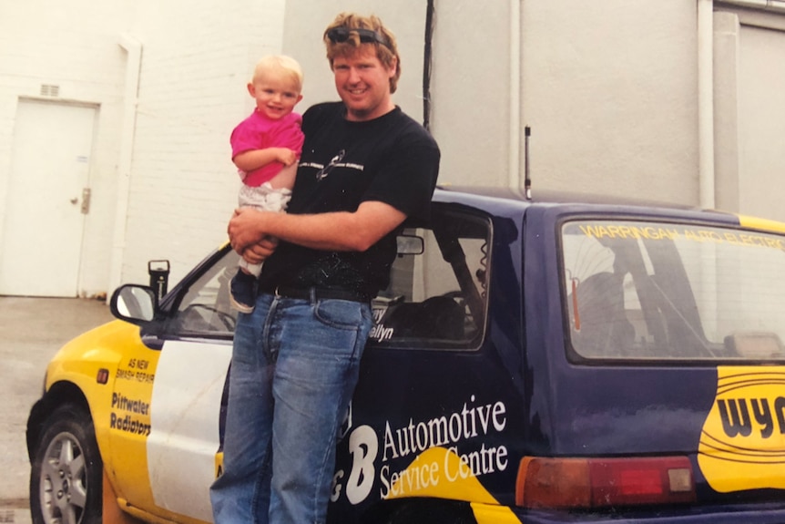 Father and baby daughter standing beside a rally car