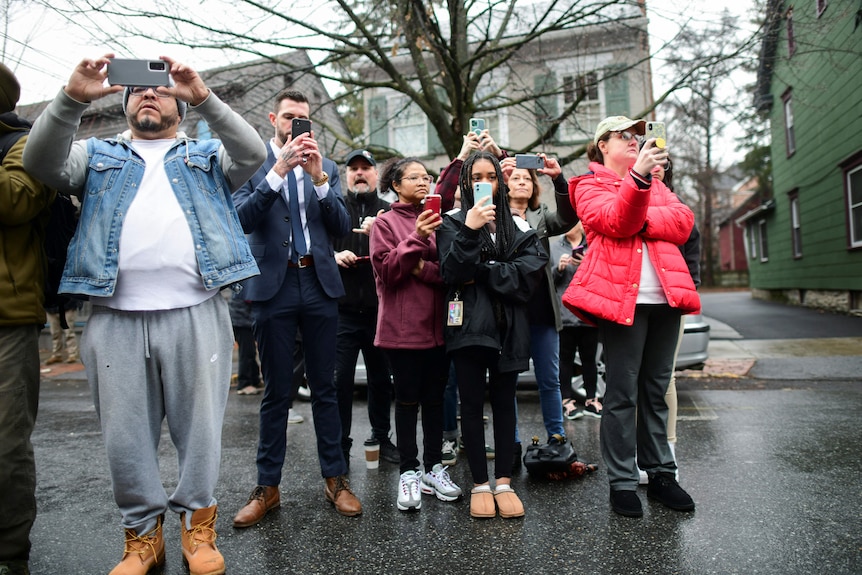A group of people stand on a street holding up their phones