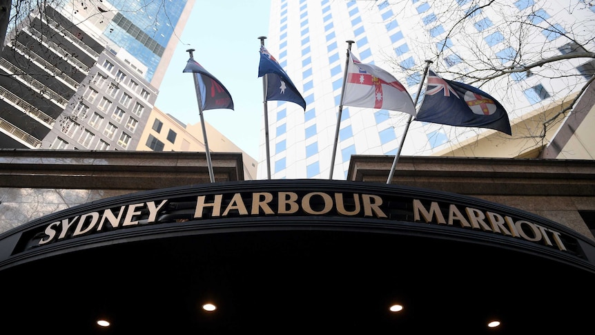 a low angle shot of a sign showing sydney harbour marriott underneath flags