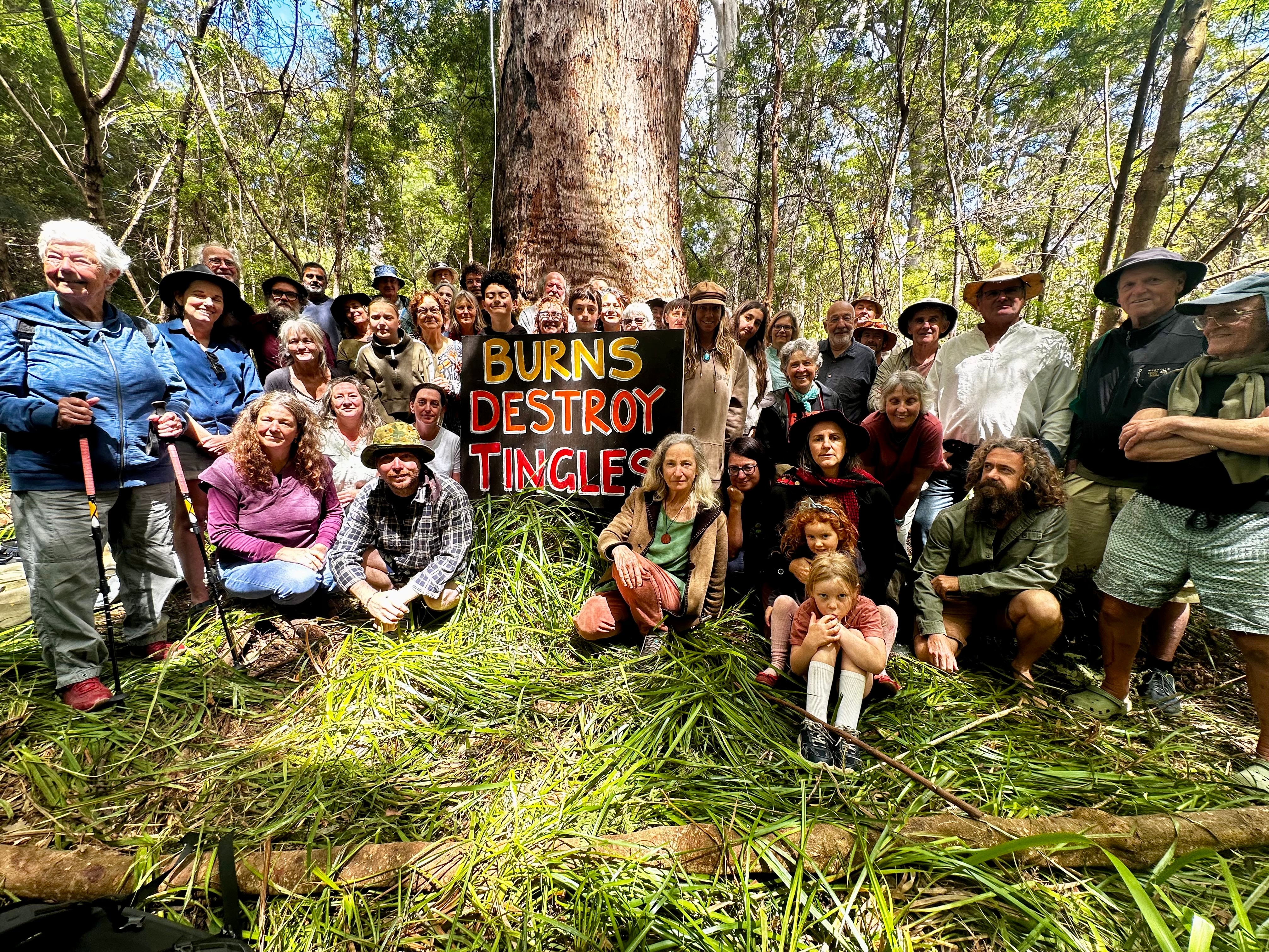 Una foto de más de 40 personas reunidas en un bosque alrededor de un cartel que dice 