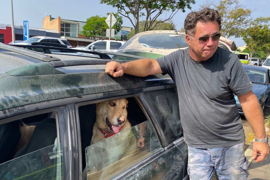 David Grant leans on his dust covered car. His dog looks out the window.