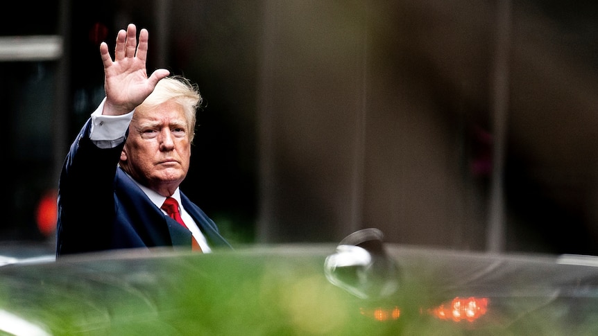 Trump waves as he exits a car.