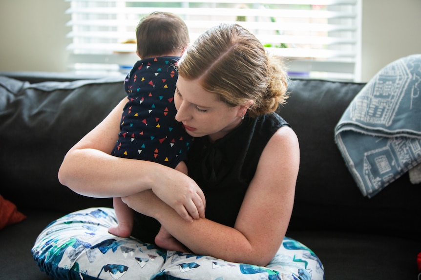 A woman looks down as she holds an infant over her shoulder.