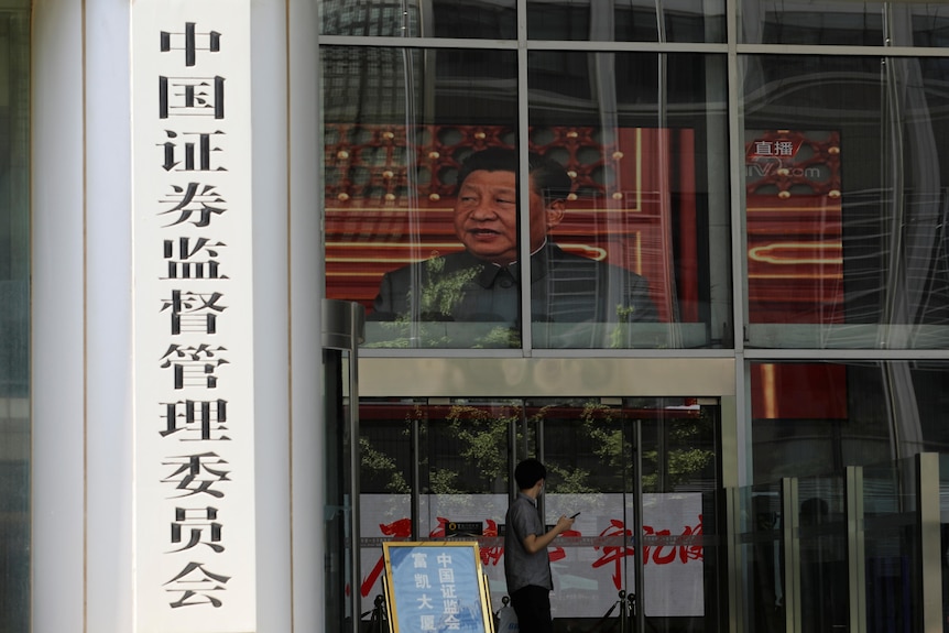 A man walks past a building with a sign for the China Securities Regulatory Commission. Inside, Xi Jinping's face is on a screen