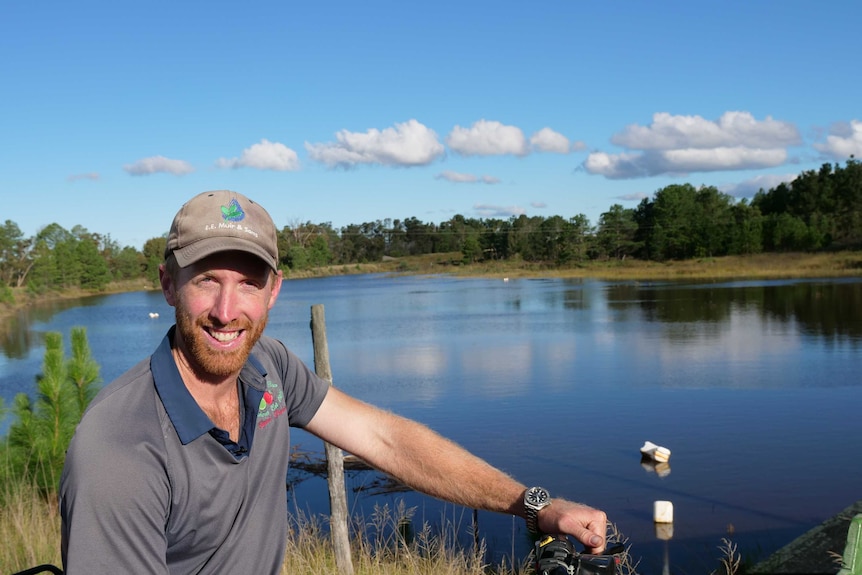 A farmer is sitting on his quad bike beside his dam.