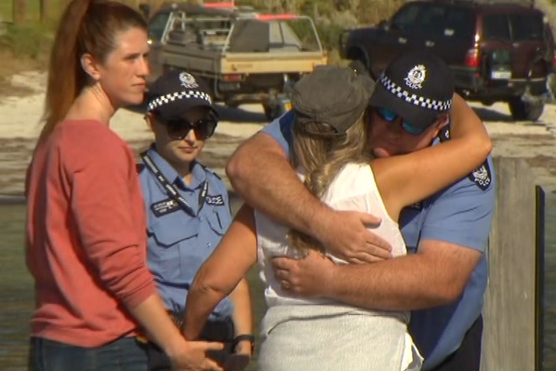 A woman holds the hand of her daughter as she is hugged on a jetty by a police officer.
