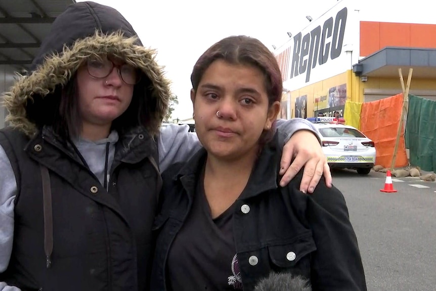 A young girl wraps her arms around another.