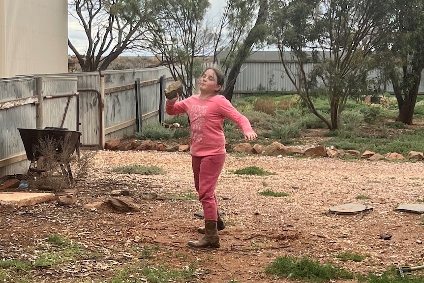 A young girl in a garden hurling a large rock, shot-put style.
