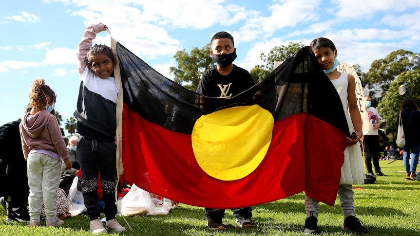 Aboriginal and Torres Strait Islander children hold Aboriginal flag at rally