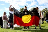 Aboriginal and Torres Strait Islander children hold Aboriginal flag at rally