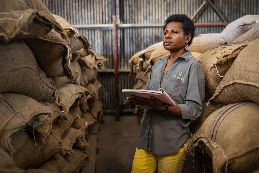 A Black woman wearing earings and holding a file inspects bags of cocoa beans