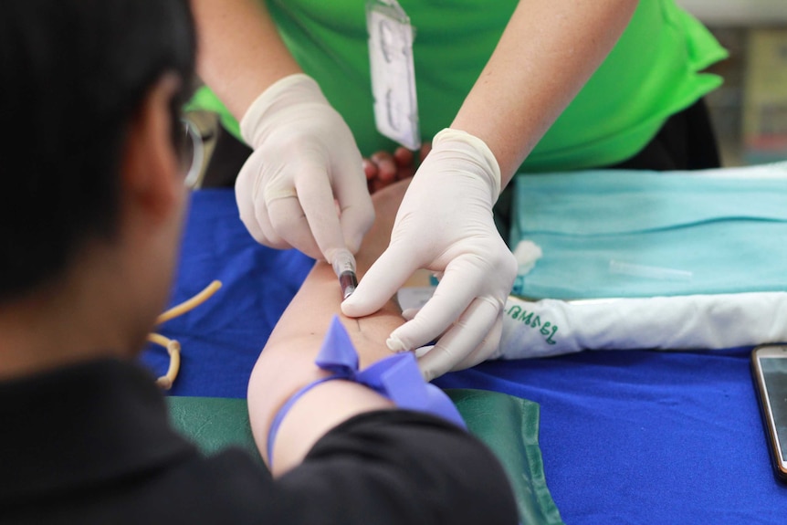 Close up of gloved hands stick a needle into a man's arm