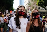 Two women wearing face masks that say WE DISSENT march among a crowd of young women on the streets of LA.