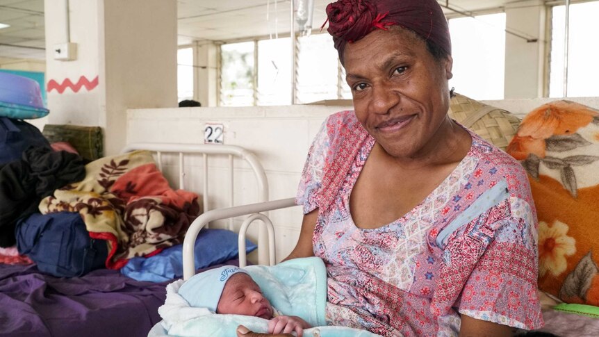 A Papua New Guinean woman lying in a hospital bed holding a newborn baby boy.