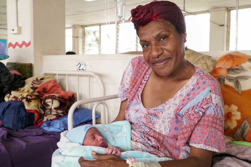 A Papua New Guinean woman lying in a hospital bed holding a newborn baby boy.