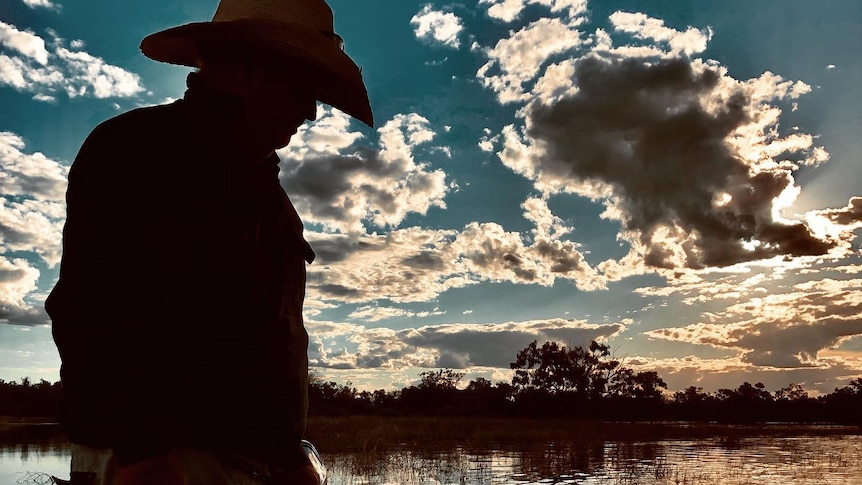 The silhouette of a man with an akubra on a speed boat in the river