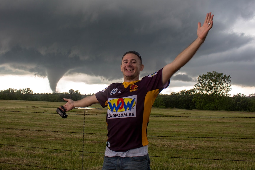 man in a broncos jersey standing triumphant with a tornado in the background