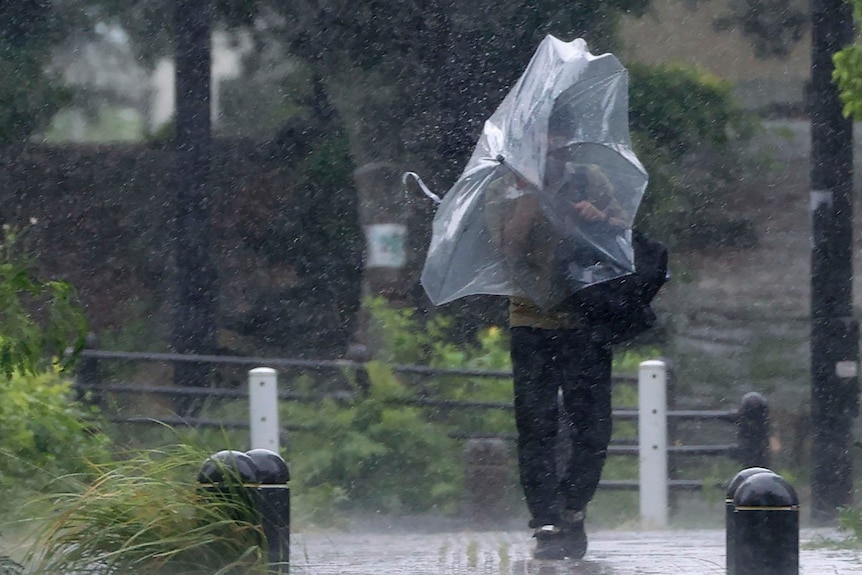 A man walks with an umbrella on a street as winds force the umbrella inside out. 