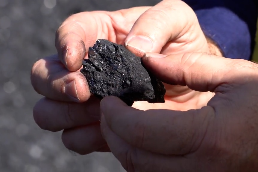 Close up photo of two hands holding a lump of coal