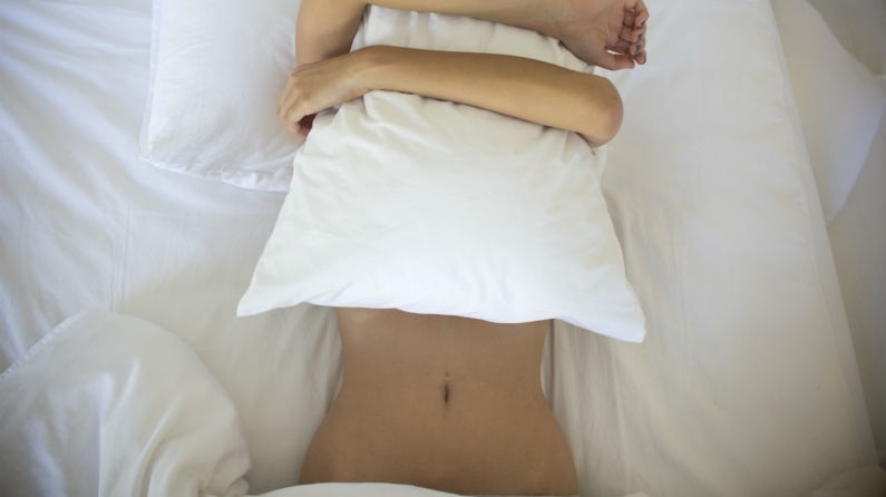 A woman alone in bed hugging a pillow to her face.