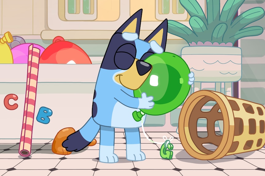 A still of Bluey in a bathroom hugging a green balloon. More balloons are in the bathtub behind her.