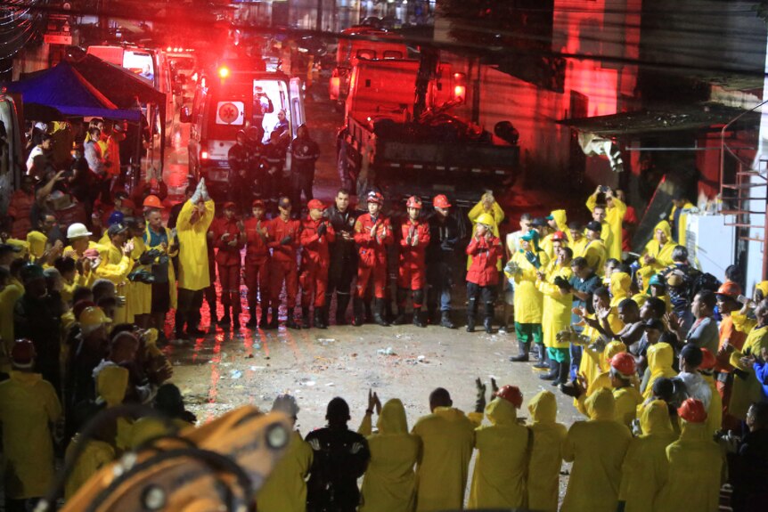 Rescuers in orange and yellow clothing stand around at nightin a circle. 