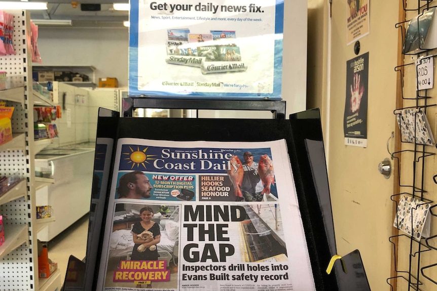 A newsstand for the local  newspaper at a convenience shop.