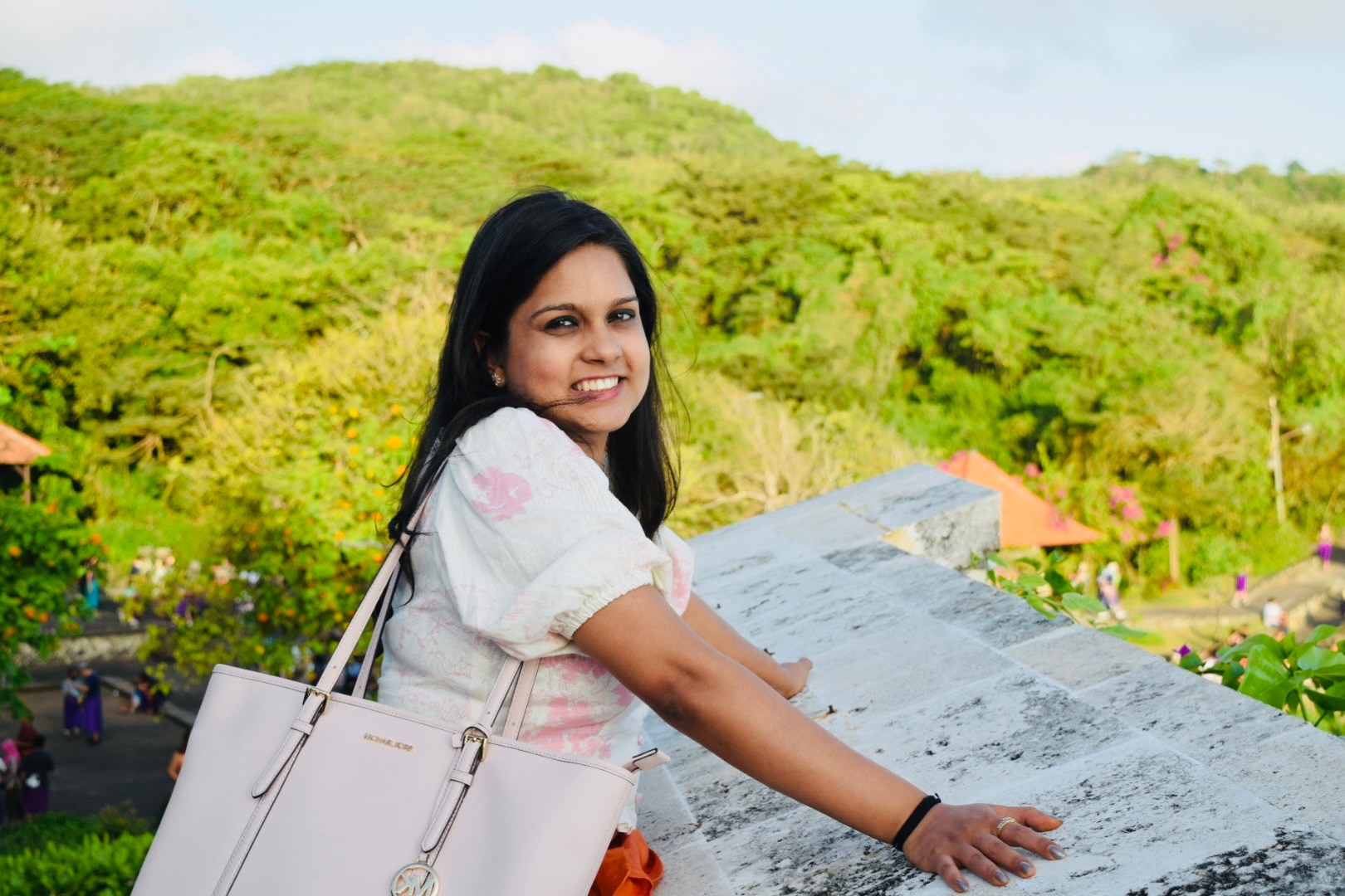A woman smiles for the camera on a hill overlooking a small village.
