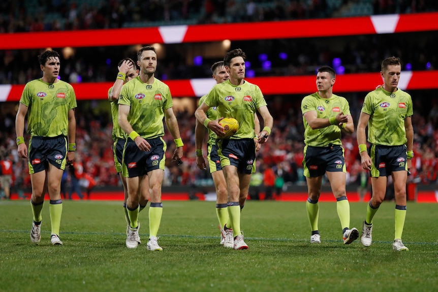 A group of umpires walk off the SCG at the end of an AFL match