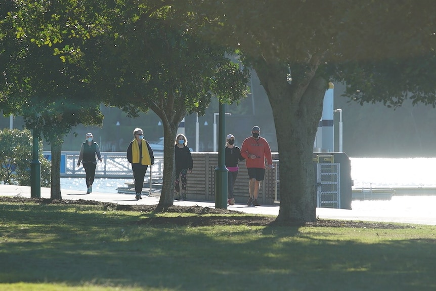 People walk along the Brisbane River at New Farm wearing face masks.