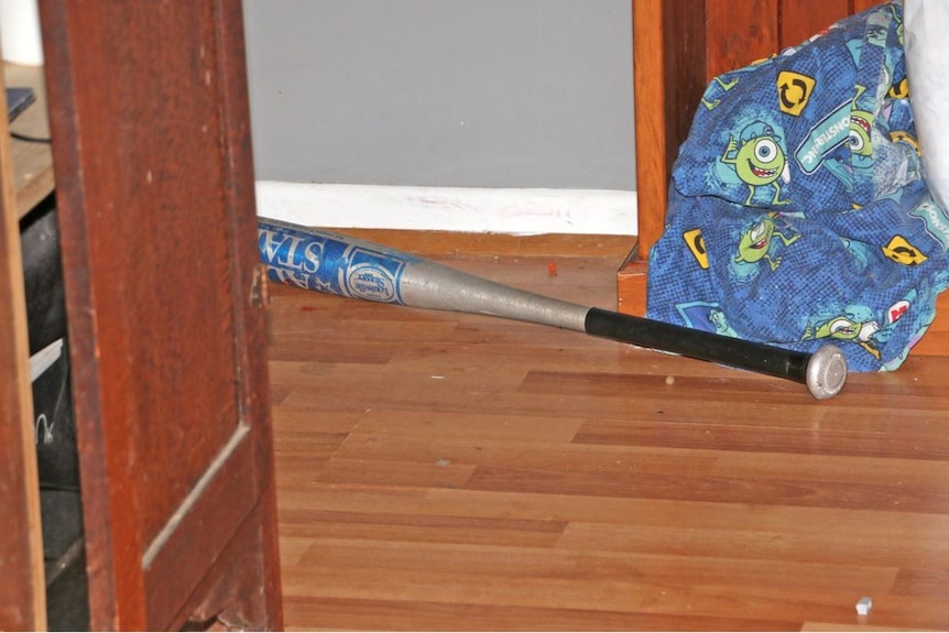 A baseball bat lays on the hardwood floor of a home