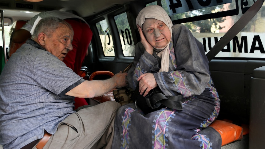 Older man and woman with rubble dust on their face inside a vehicle 