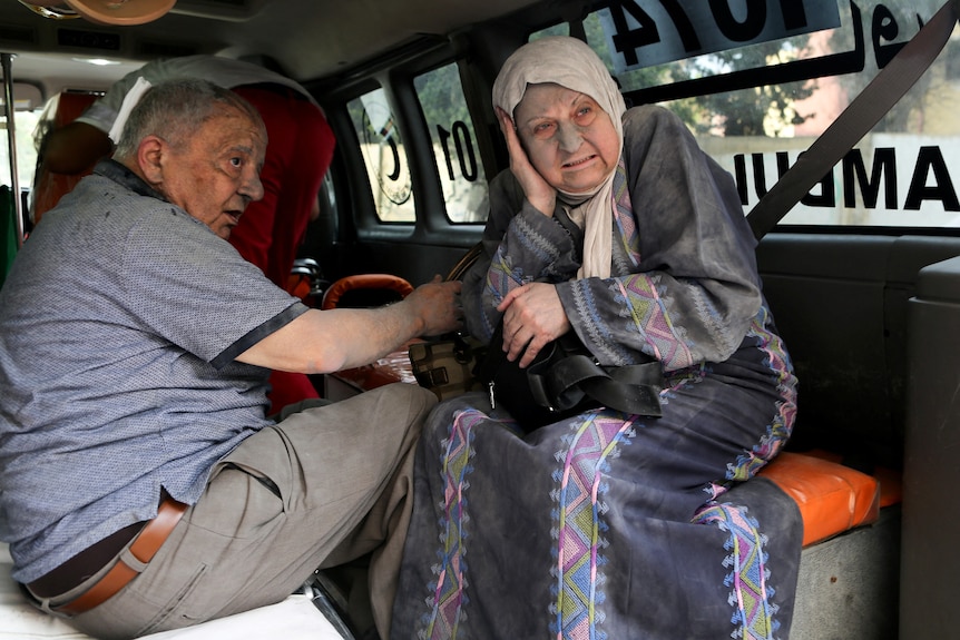 Older man and woman with rubble dust on their face inside a vehicle 