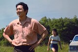 A still from the film Minari with Steven Yeun, patriarch of a family in the foreground, his wife and two kids in the background