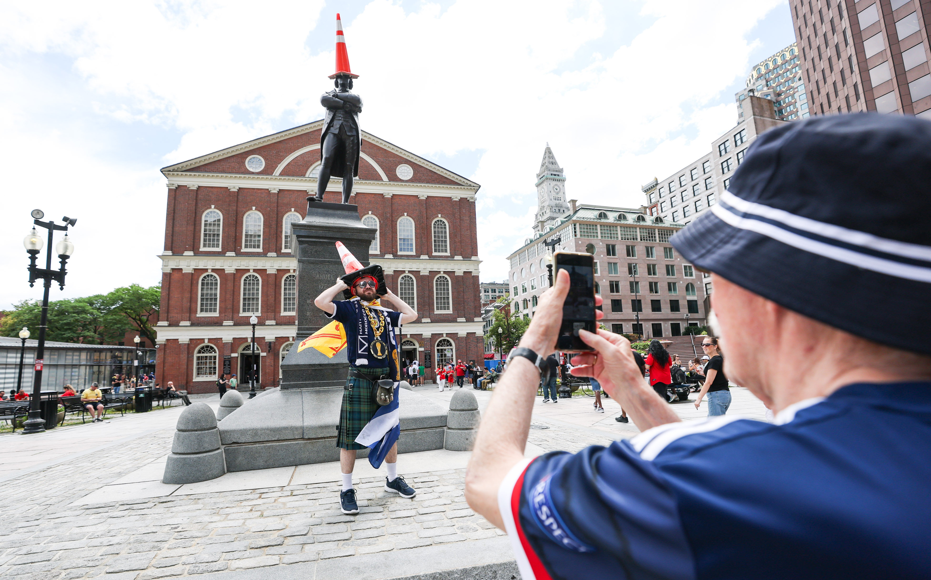 A Scottish man wearing a traffic cone getting a photo in front of a statue with a traffic cone on it
