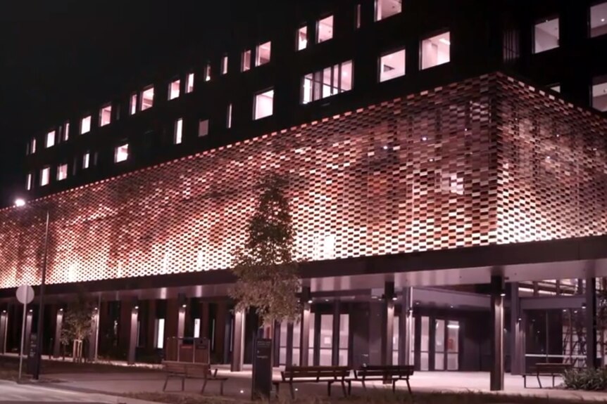 A large building lit up at night, with a metallic structure on the facade featuring Indigenous designs.