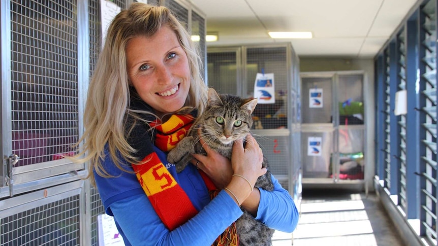 A woman in a Crows scarf holds a cat.