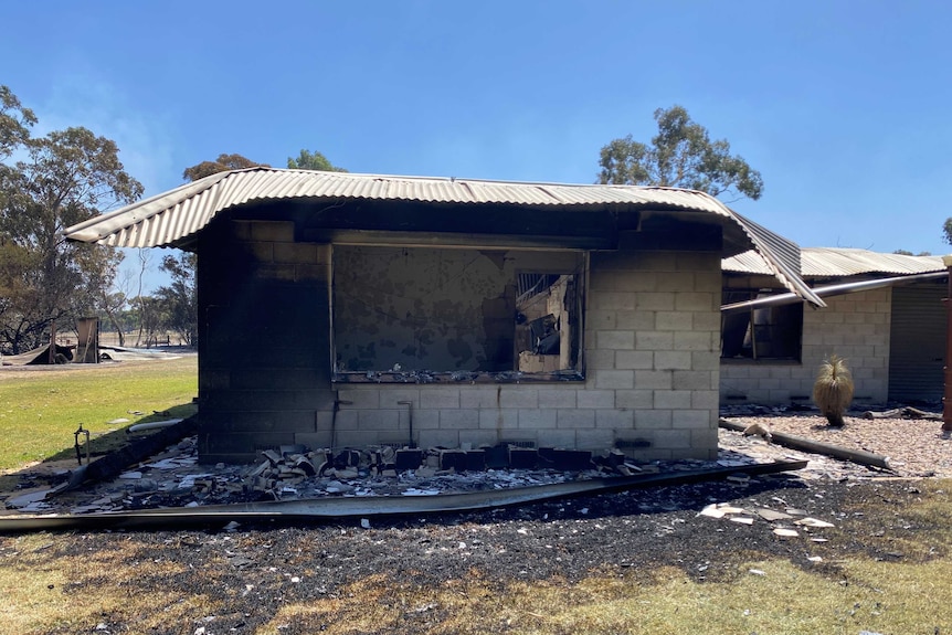 A house completely blackened by fire, with collapsed roof and blown windows.