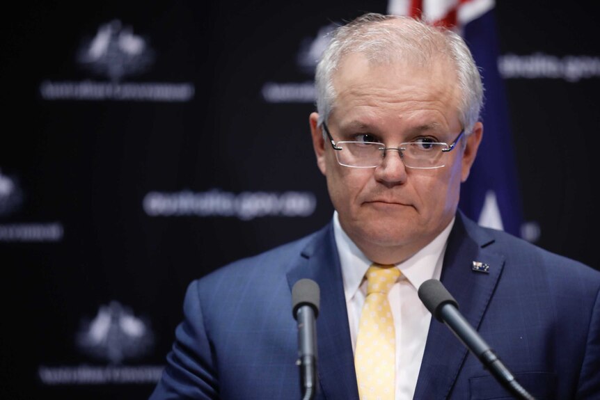 Scott Morrison stands in front of microphone with an Australian flag behind him