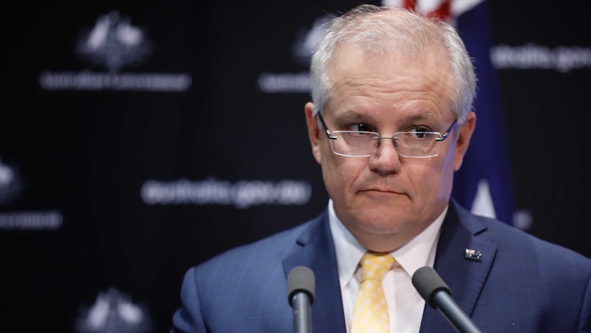 Scott Morrison stands in front of microphone with an Australian flag behind him