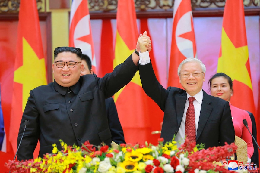 North Korean leader Kim Jong-un and Vietnamese President Nguyen Phu Trong clasp hands in front of their respective flags.