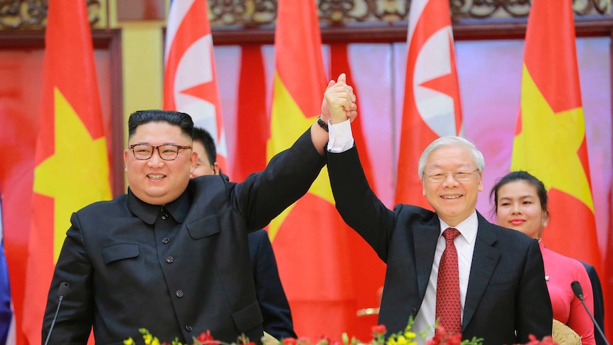 North Korean leader Kim Jong-un and Vietnamese President Nguyen Phu Trong clasp hands in front of their respective flags.